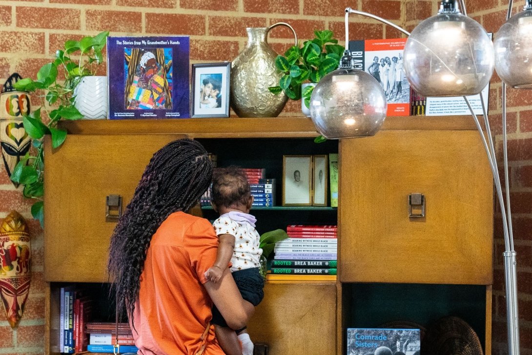 A woman holding a baby examines objects in the living room created for the Black Future Newsstand exhibit in Los Angeles