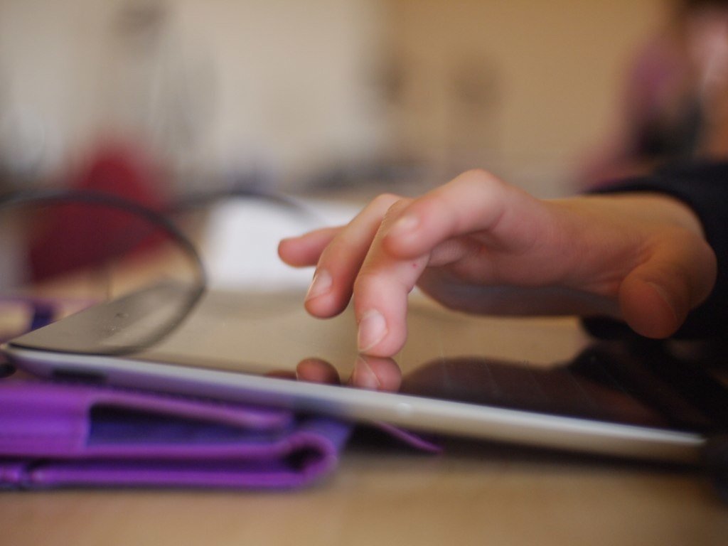 Hand touching iPad propped up on a desk