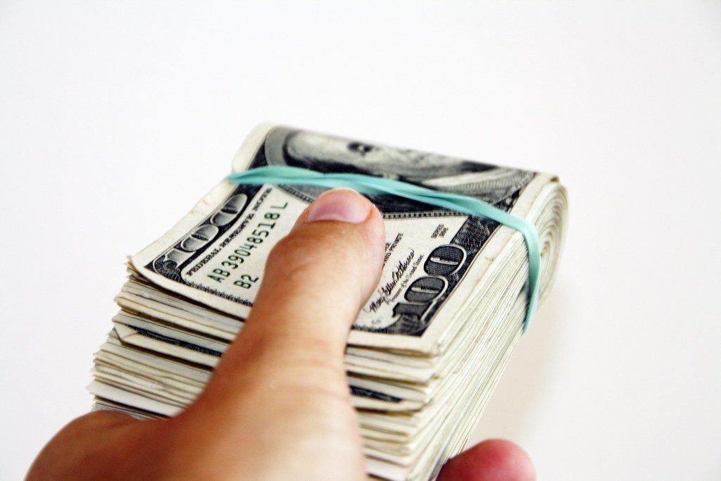 A hand holding a wad of $100 bills