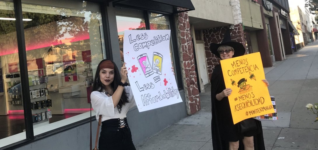 A woman dressed as a pirate and a woman dressed as a witch pose with anti-merger signs