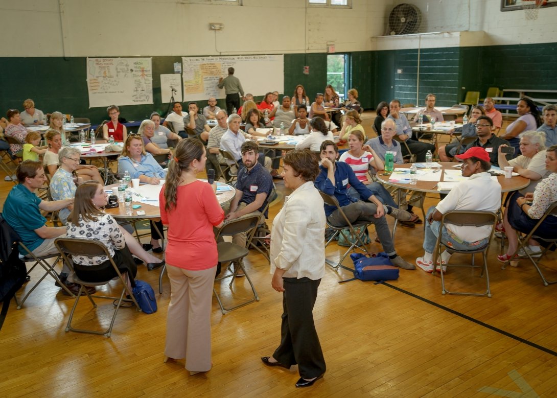 Two people standing and other people sitting at tables in the background