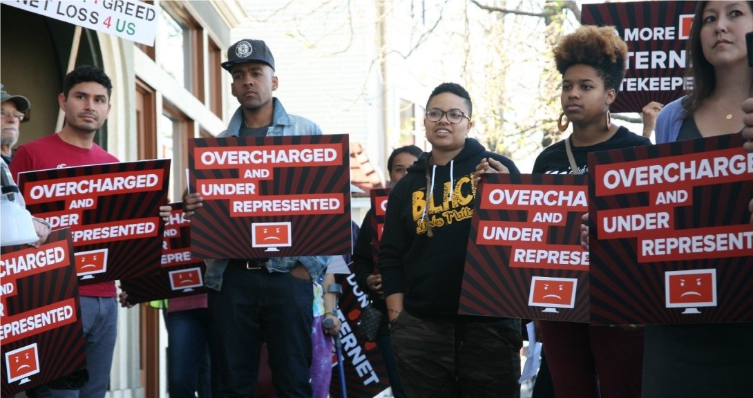 Activists holding posters reading "Overcharged and underrepresented"
