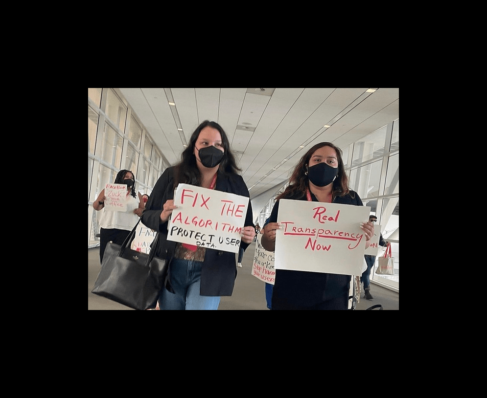 Rose Lang-Maso and another activist holding signs reading "Fix the algorithm" and "Real transparency now"