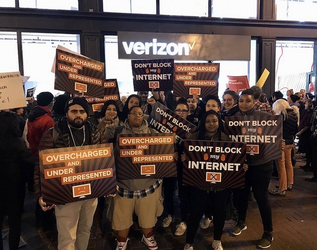 San Francisco protesters holding "Overcharged and underrepresented" and "Don't block my internet" signs