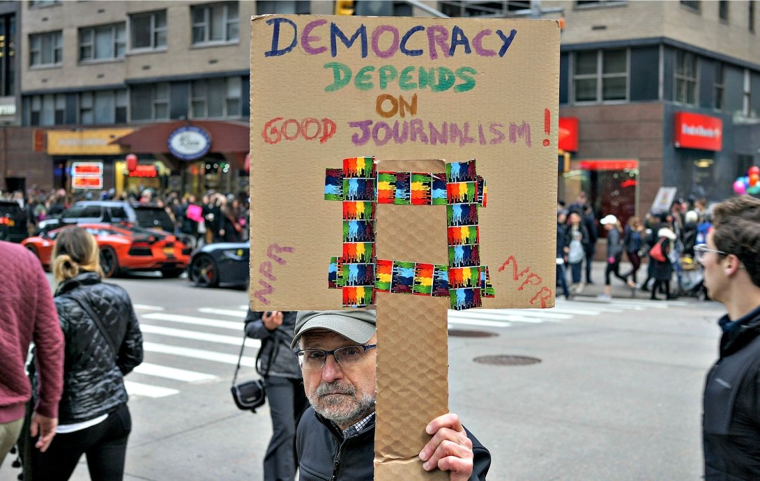 Man holding sign saying "Democracy depends on good journalism"