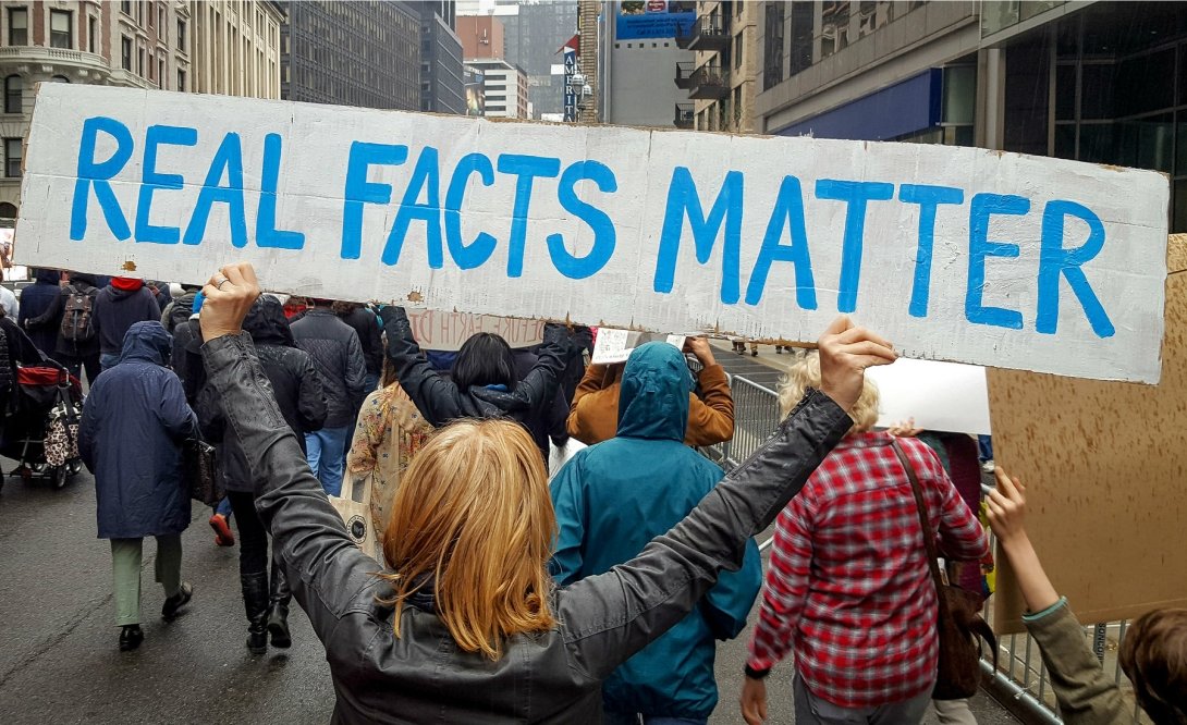 Activist holding sign reading "Real Facts Matter"
