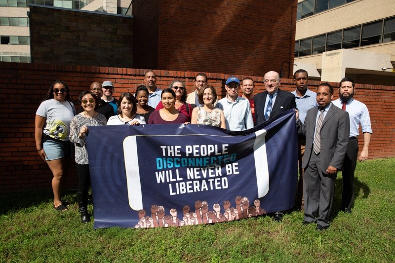 Group of people holding banner reading "The People Disconnected Will Never Be Liberated"