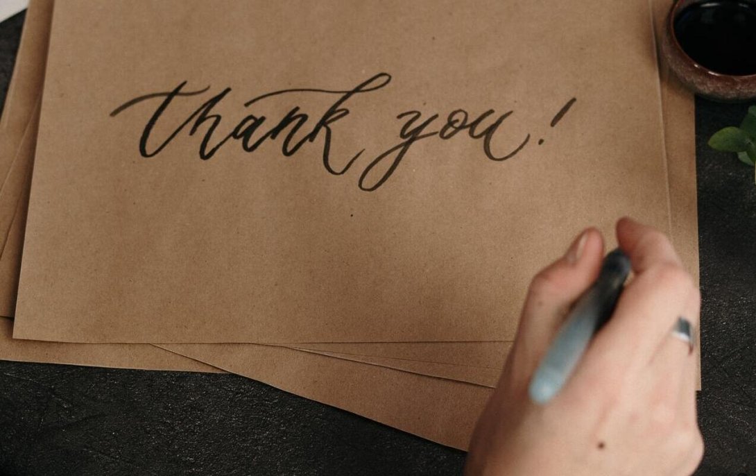 Person writing "thank you!" on a piece of brown paper