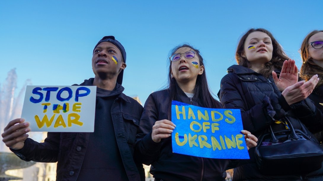 Three protesters holding signs reading "Stop the war" and "Hands off Ukraine"