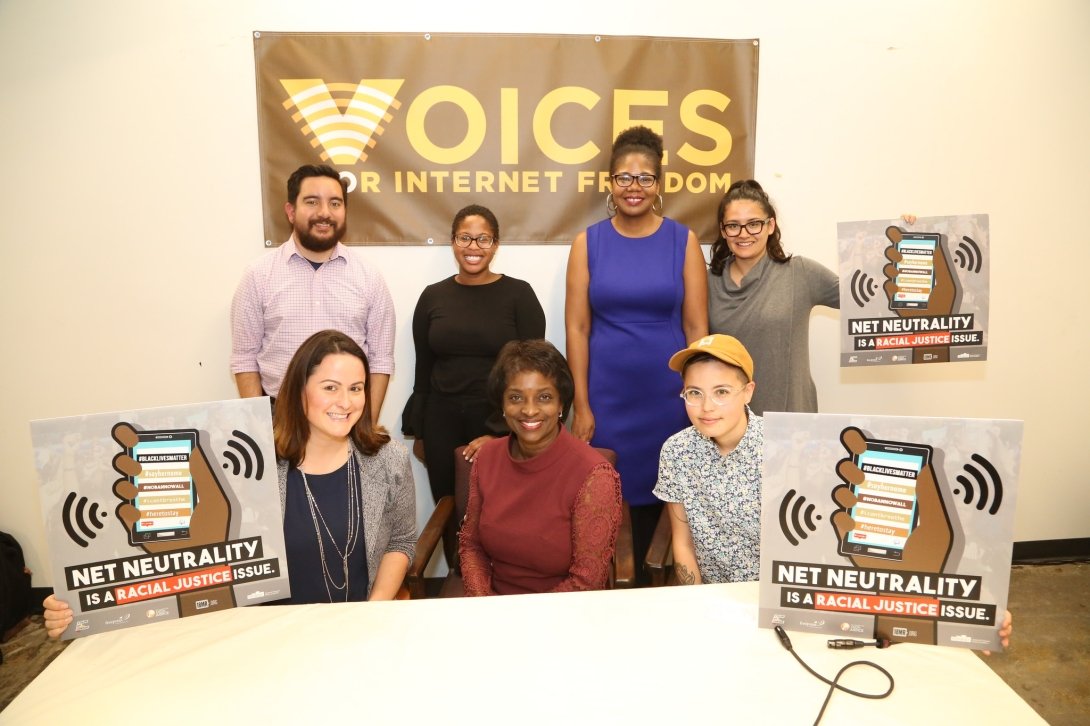 Seven people seated before a "Voices for Internet Freedom" sign